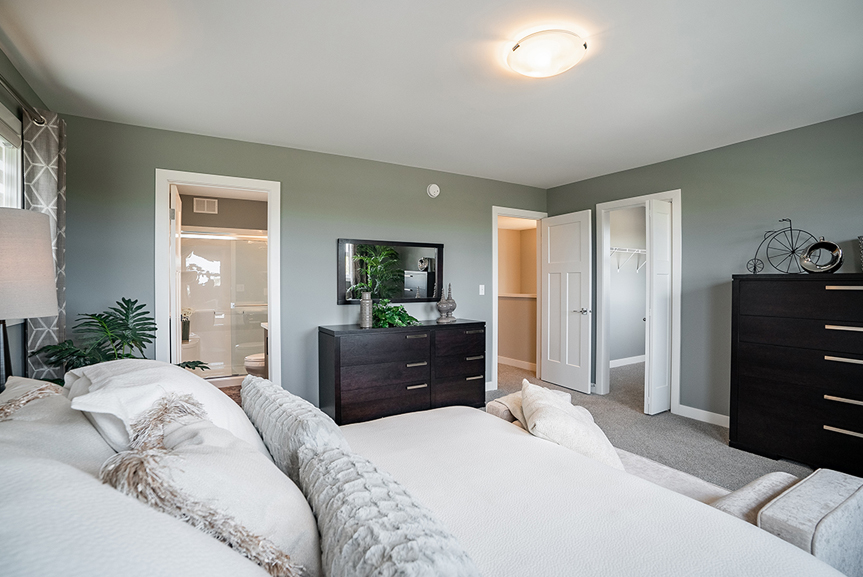 master bedroom with green walls, white casing and baseboards and view of the walk-in closet and ensuite the preston broadview homes winnipeg