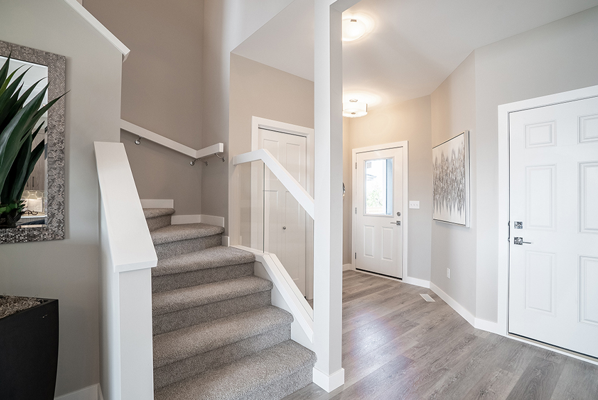 foyer with vinyl plank flooring, beige walls, staircase with white maple railing with glass inserts the preston broadview homes winnipeg